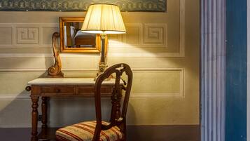 A wooden desk with a mirror, a lamp, and a chair in a room with decorative molding and a painting on the wall.
