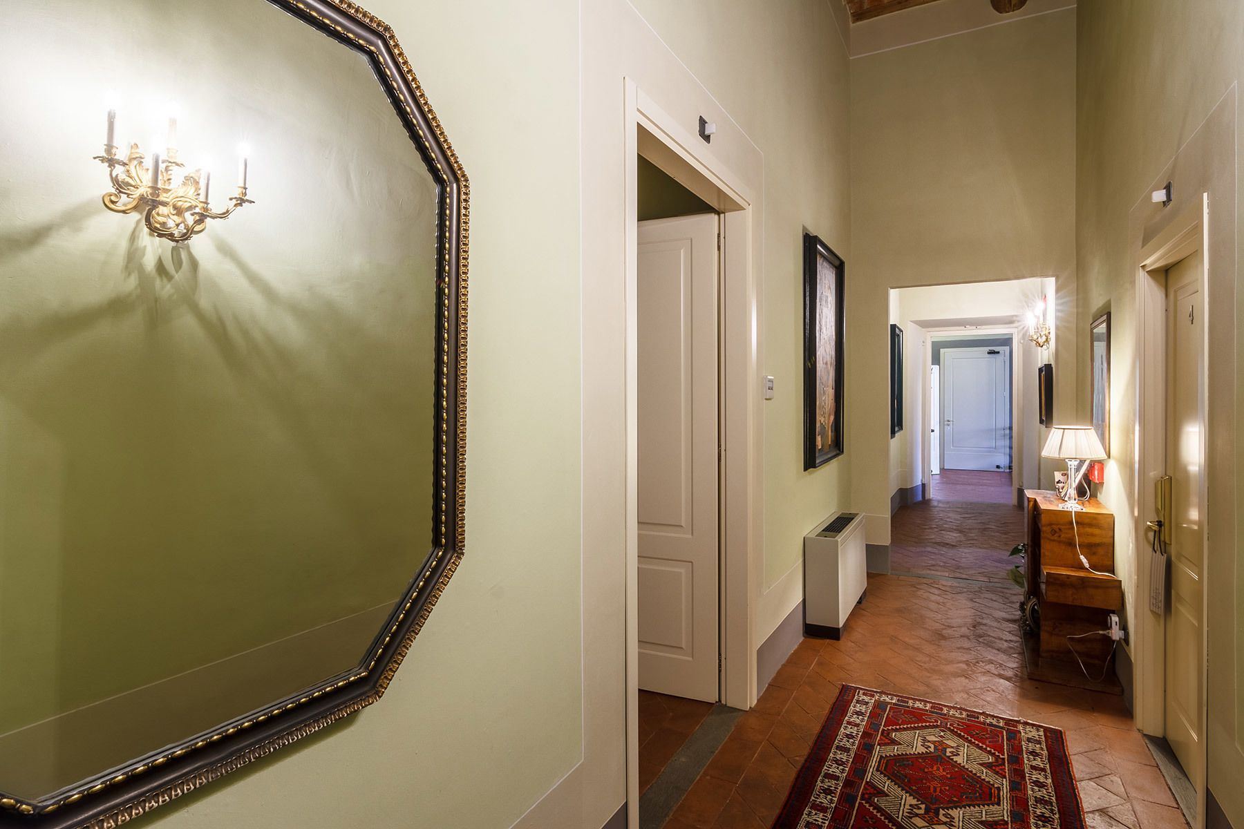 A hallway with a large mirror, a chandelier, and a rug.