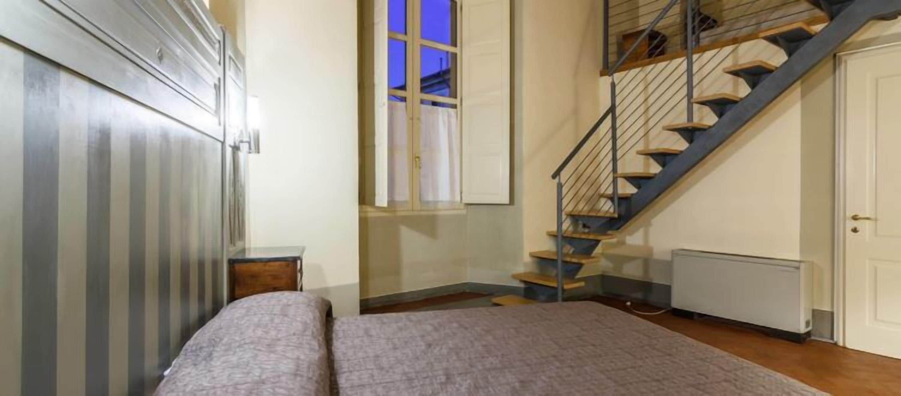 Un dormitorio con cama, ventana, escalera y radiador.