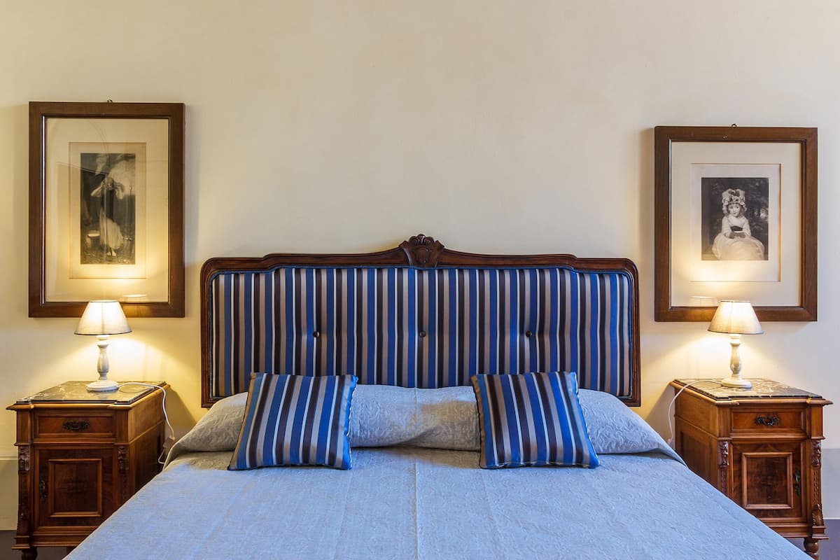 A neatly made bed with striped bedding, flanked by two bedside tables with lamps, and framed pictures on the walls.