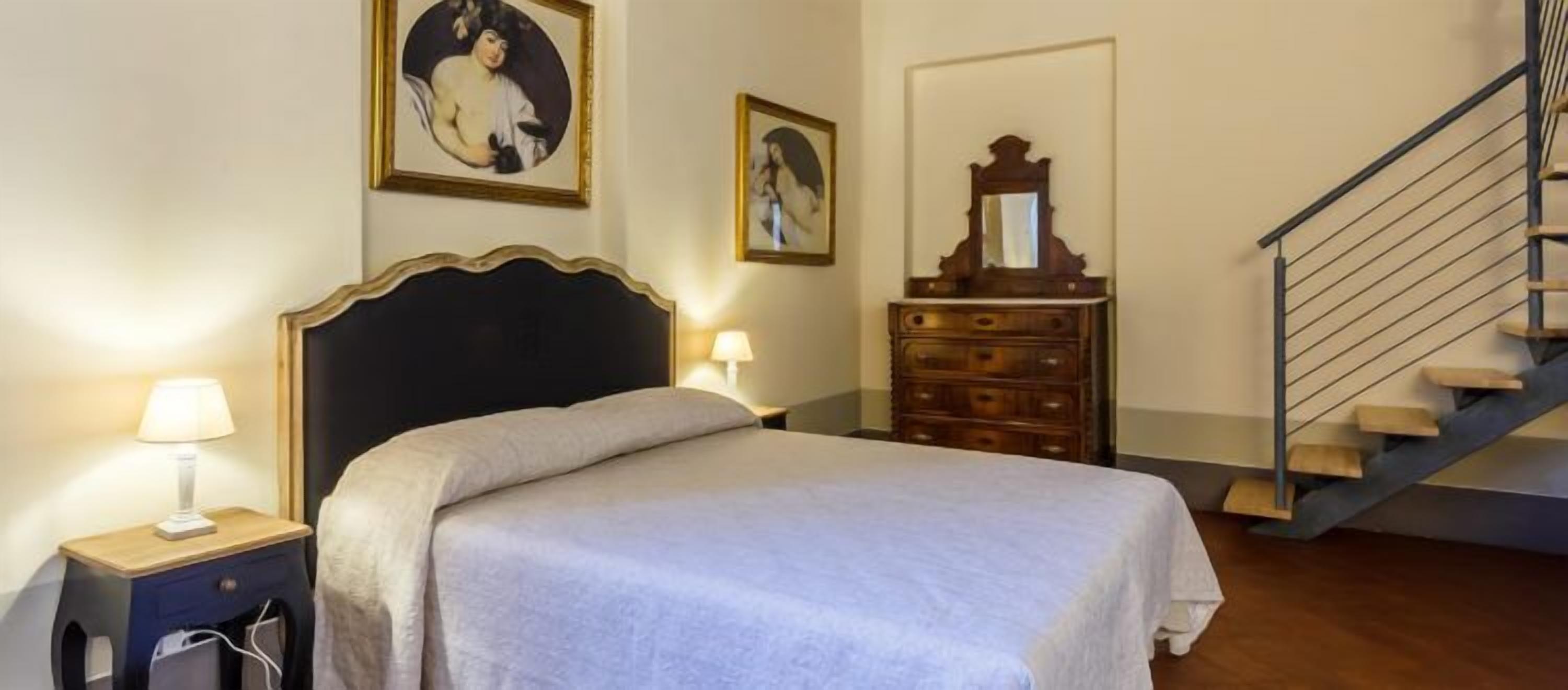A bedroom with a bed, nightstands, a dresser, a mirror, and a staircase.