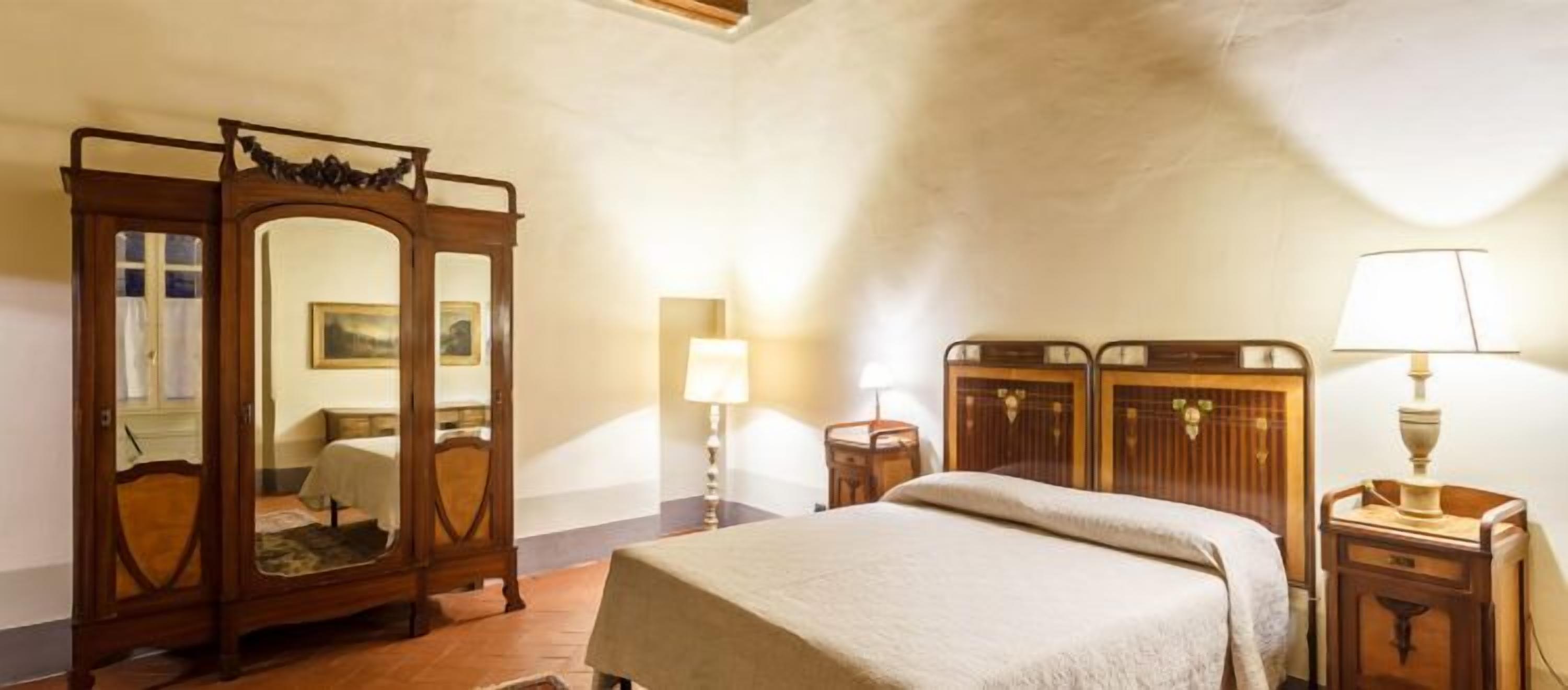 Une chambre à coucher comprenant un lit, une armoire en bois, un miroir et deux tables de chevet avec des lampes.