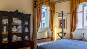 Un dormitorio con una cama con dosel, un aparador de madera oscura con objetos de cerámica y una ventana con cortinas.