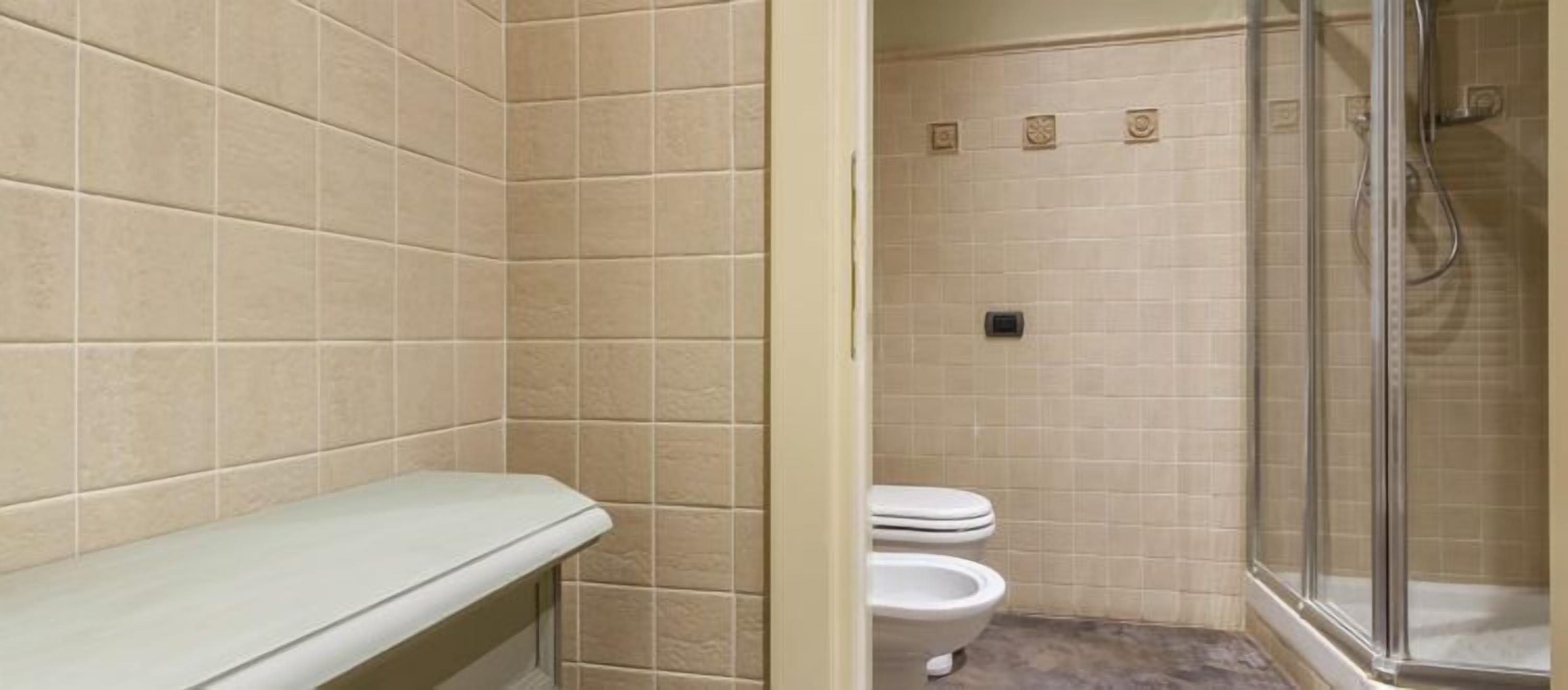 Une salle de bain avec des carreaux de couleur beige, des toilettes blanches et un espace douche.