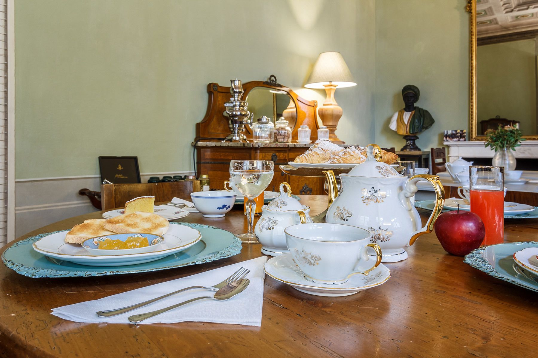 Une table à manger avec des assiettes, des couverts, une théière, un pichet et un fruit.
