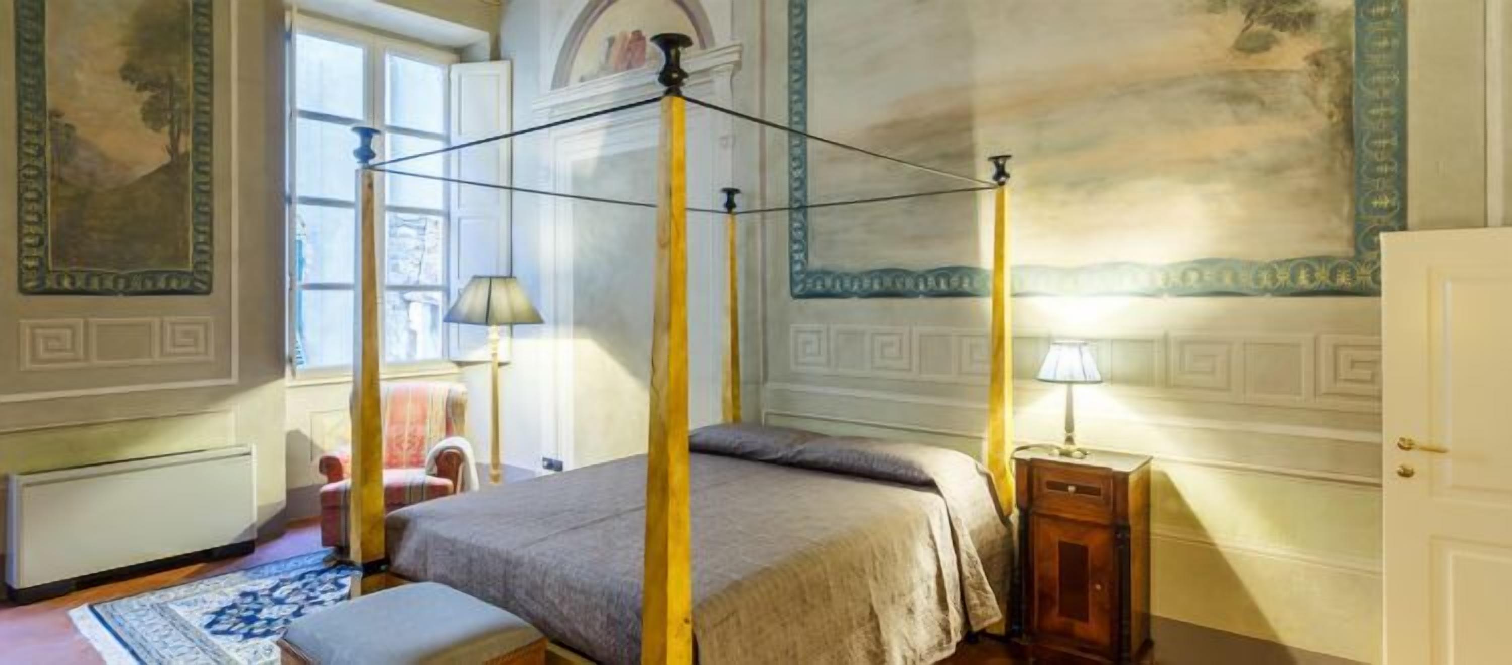 Una cama con dosel en una habitación con un ventanal grande, un radiador y una lámpara en una mesita de noche.