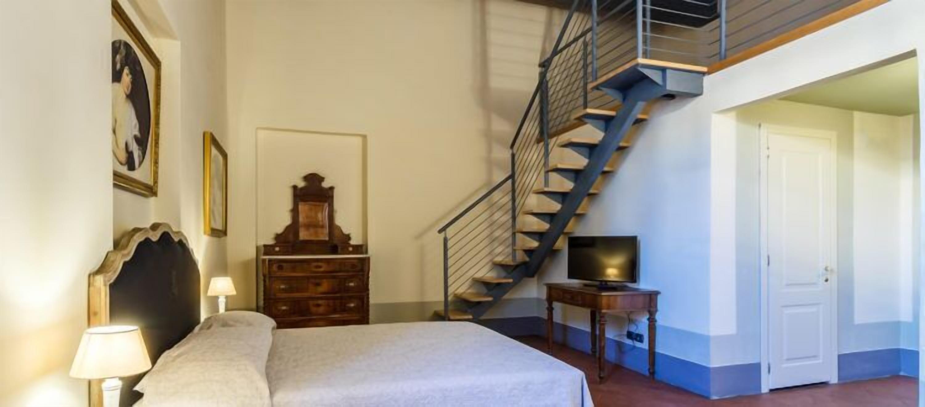 A bedroom with a bed, dresser, TV, and a staircase.
