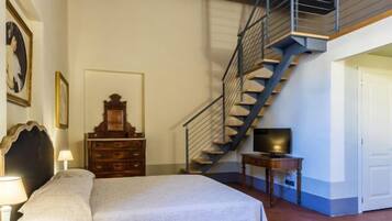 A bedroom with a bed, dresser, TV, and a staircase.
