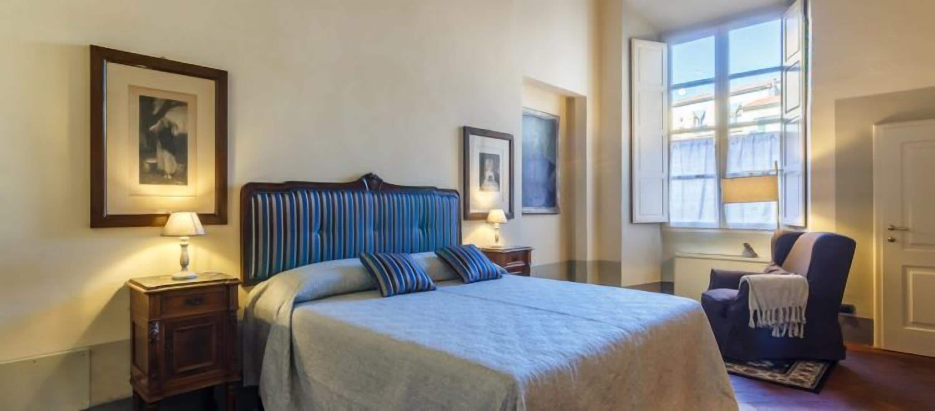 A hotel room with a large bed, two bedside tables with lamps, a chair, and a window with a view.
