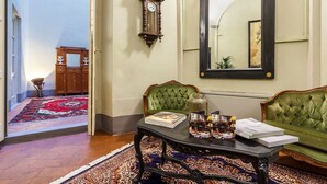 Una habitación con un sofá verde, una mesa con revistas, un reloj y un espejo en la pared.