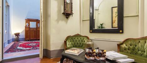 A room with a green sofa, a table with magazines, a clock, and a mirror on the wall.