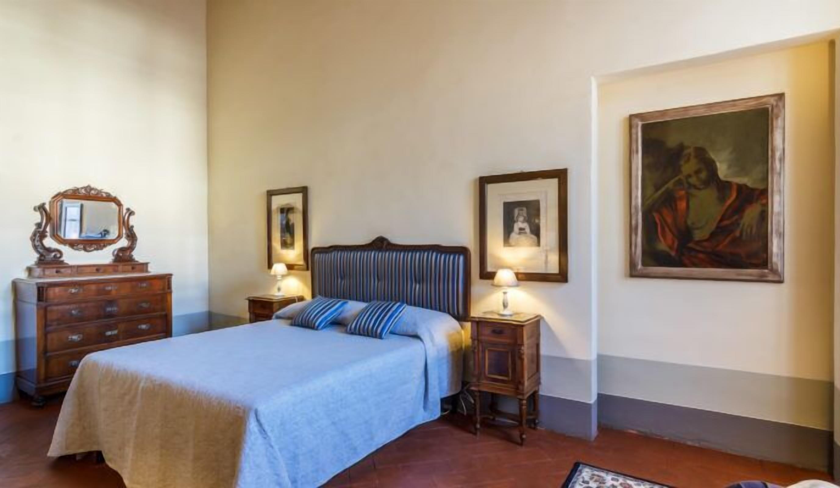Un dormitorio ordenado con una cama, dos mesitas de noche con lámparas, un aparador y cuadros enmarcados en las paredes.