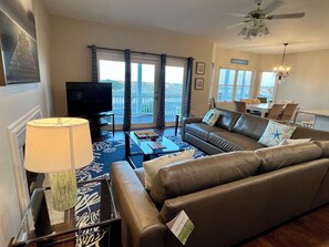 A living room with a sofa, a coffee table, a TV, and a balcony with curtains.