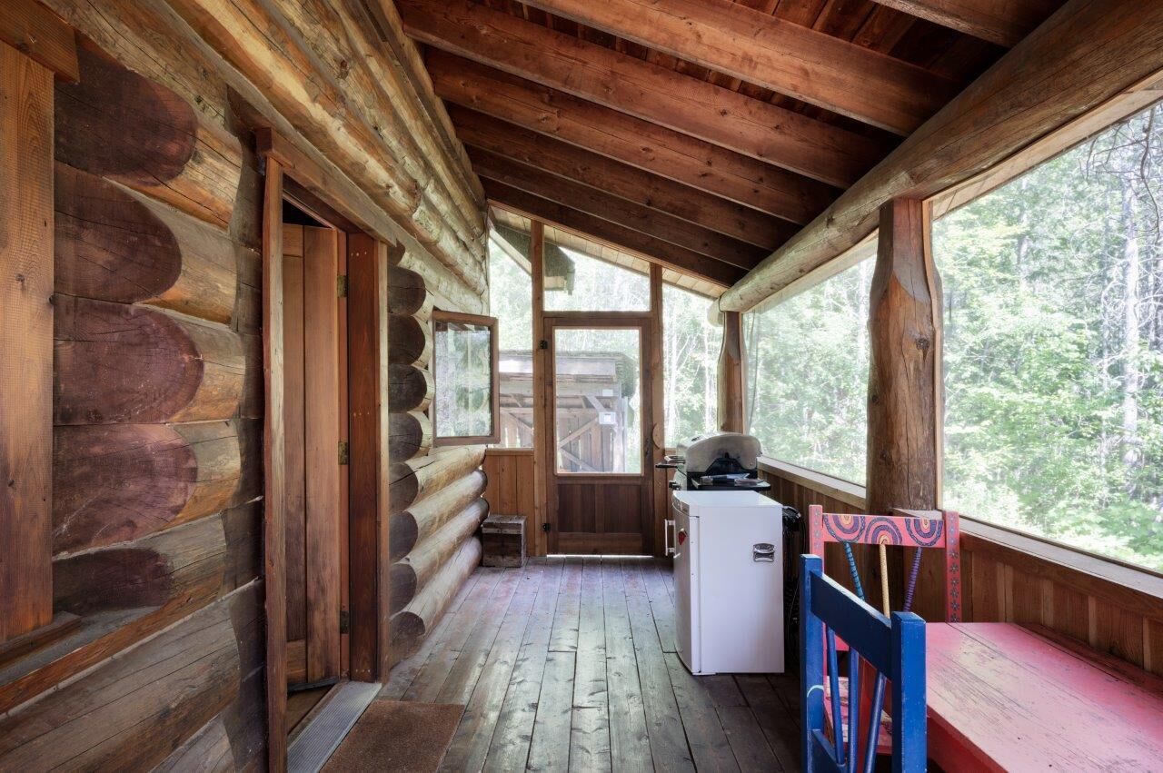 Interno di una baita in legno, con pavimento in legno, angolo cottura e ampie finestre che si affacciano sulla foresta.