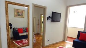 A living room with a sofa, a TV, a mirror, and a red and white patterned rug. - Excelente Apartamento Em Copacabana (Rio de Janeiro)