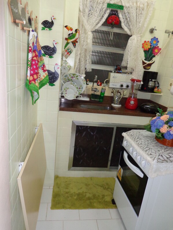 A compact kitchen with a sink, stove, and a small window with curtains. - Excelente Apartamento Em Copacabana (Rio de Janeiro)