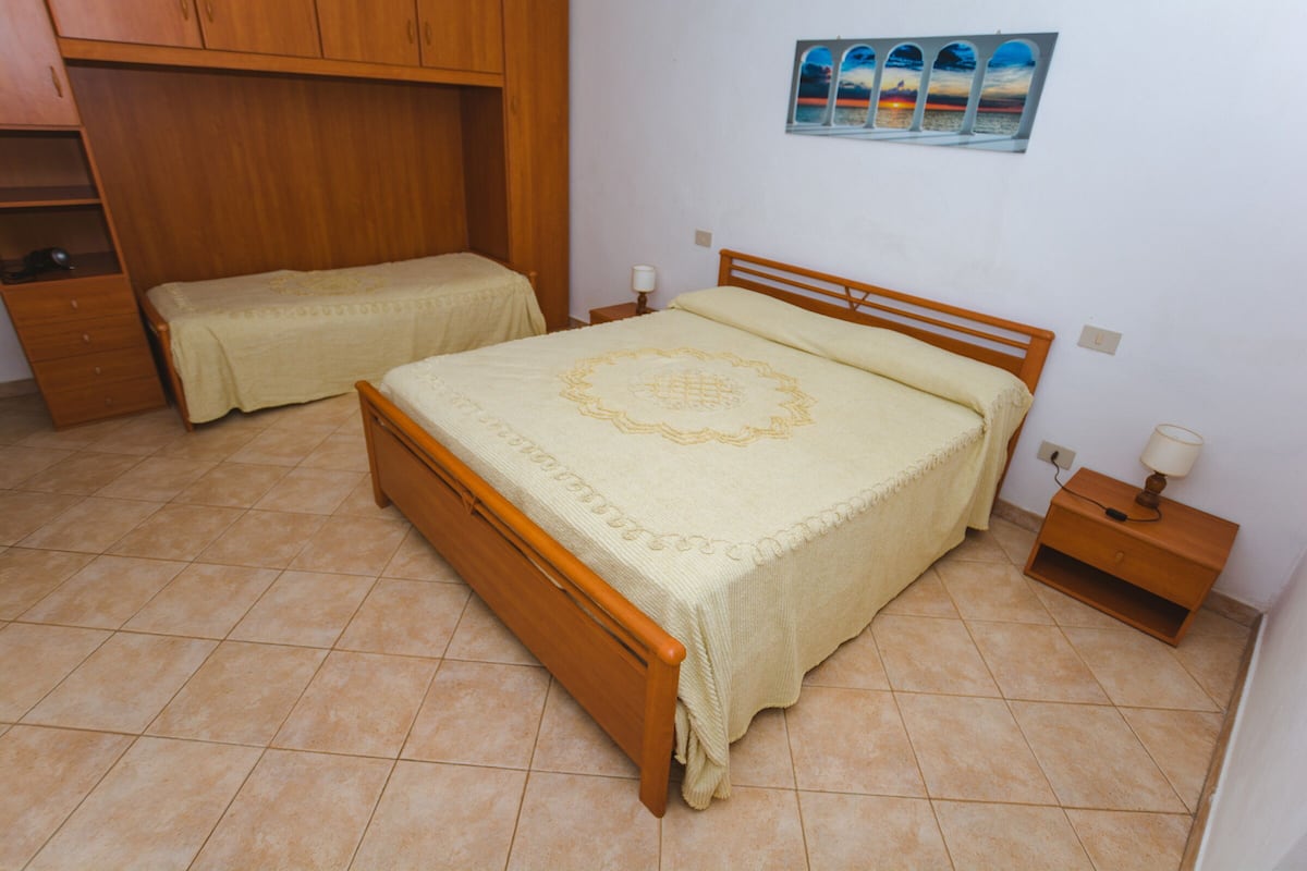 A bedroom with two single beds, wooden furniture, a tiled floor, and a wall-mounted picture.