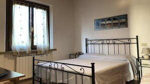 A bedroom with a single bed, a window with curtains, a radiator, a wall-mounted picture, and a bedside table with a lamp. - Agriturismo Ferri di Ferri Donatella (Bibbona)
