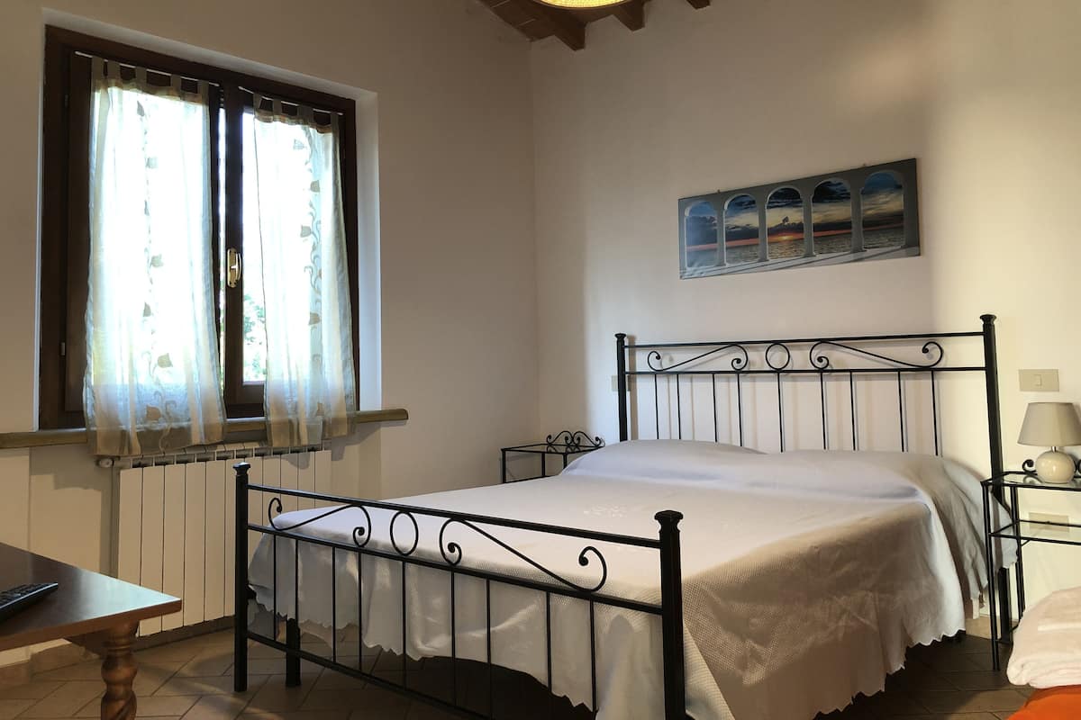 A bedroom with a single bed, a window with curtains, a radiator, a wall-mounted picture, and a bedside table with a lamp.