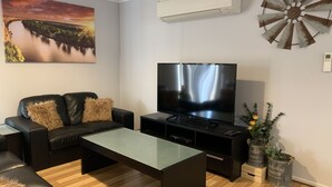Ein Wohnzimmer mit einer schwarzen Ledersofa, einem Glastisch, einem Flachbildfernseher und Dekorationselementen, darunter eine Windmühle und Topfpflanzen.