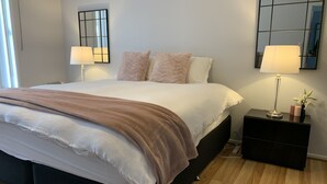 Ein modernes Schlafzimmer mit einem großen Bett, zwei Nachttischlampen, einem Spiegel und einem Nachttisch mit Lampe.