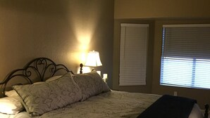 Un dormitorio con cama, lámpara de noche y ventana con persianas.