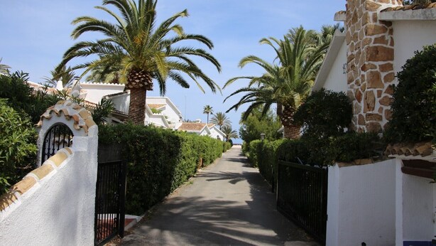 A narrow street lined with palm trees and white buildings with stone facades. - Villa LA TARDE 1ª Línea Playa (Denia)