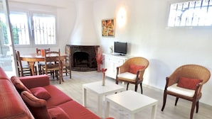 A living room with a red sofa, two wicker chairs, a white coffee table, a fireplace, and a television. - Villa LA TARDE 1ª Línea Playa (Denia)