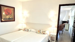 A hotel room with two beds, a nightstand with lamps, a chair, and a desk with a computer. - Villa LA TARDE 1ª Línea Playa (Denia)