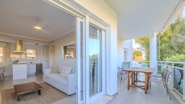 A modern apartment with a kitchen, a living area with a sofa and coffee table, and a balcony with a table and chairs. - LES PORTELLES Nº57 1ª Línea Playa (Denia)