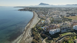 An aerial view of a coastal city with a beach, residential buildings, and a mountain in the distance. - LES PORTELLES Nº57 1ª Línea Playa (Denia)