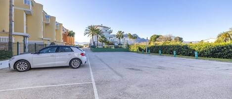 A white car parked on a street with buildings and palm trees in the background.
