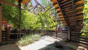 An outdoor patio area with a wooden pergola, gravel pathways, and various plants. - Sleek Baca Railyard Gem by Cafecito w/ Patio, Laundry, Full Kitchen (Santa Fe)