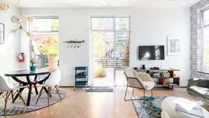 A modern living room with a dining area, a TV, and a bookshelf. - Sleek Baca Railyard Gem by Cafecito w/ Patio, Laundry, Full Kitchen (Santa Fe)