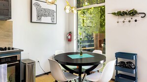 A modern kitchen with a dining area, a black and white cityscape artwork, a hanging light fixture, and a view of greenery through the window. - Sleek Baca Railyard Gem by Cafecito w/ Patio, Laundry, Full Kitchen (Santa Fe)