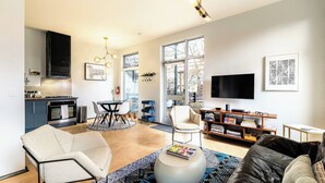 A modern living room with a sofa, a coffee table, and a TV. There is a kitchen area with cabinets and a dining table. - Sleek Baca Railyard Gem by Cafecito w/ Patio, Laundry, Full Kitchen (Santa Fe)