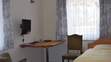 A hotel room with a bed, a desk with a computer, a chair, and a window with curtains.