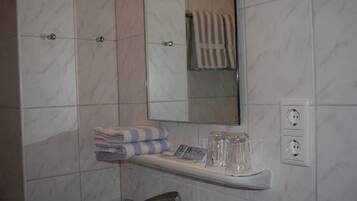 Un baño con pared de mármol, un lavabo con grifo, un perchero, un espejo y una repisa con vasos y una toalla.