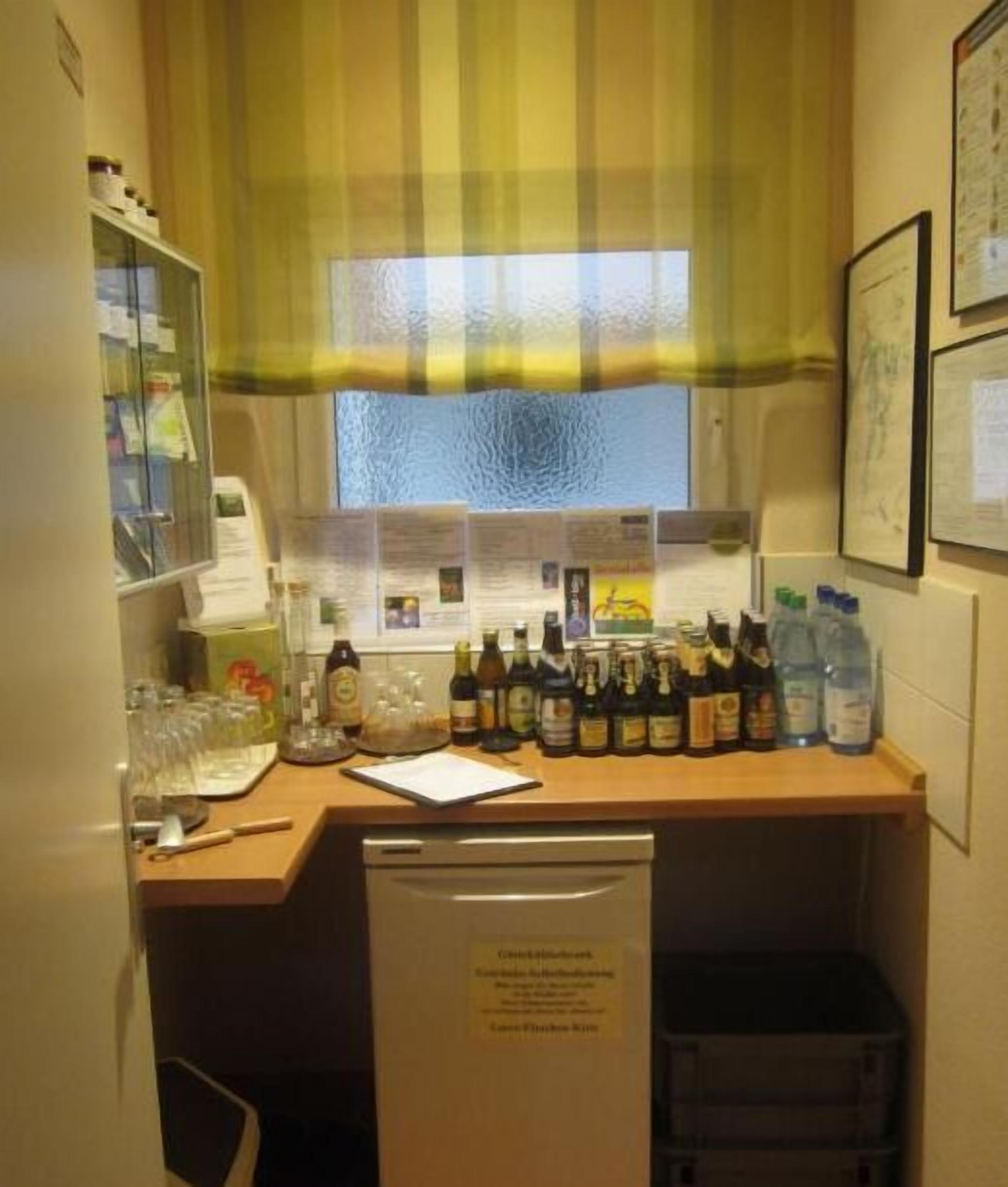 A small kitchenette with a wooden countertop, various bottles, a dishwasher, and a window with a striped curtain.