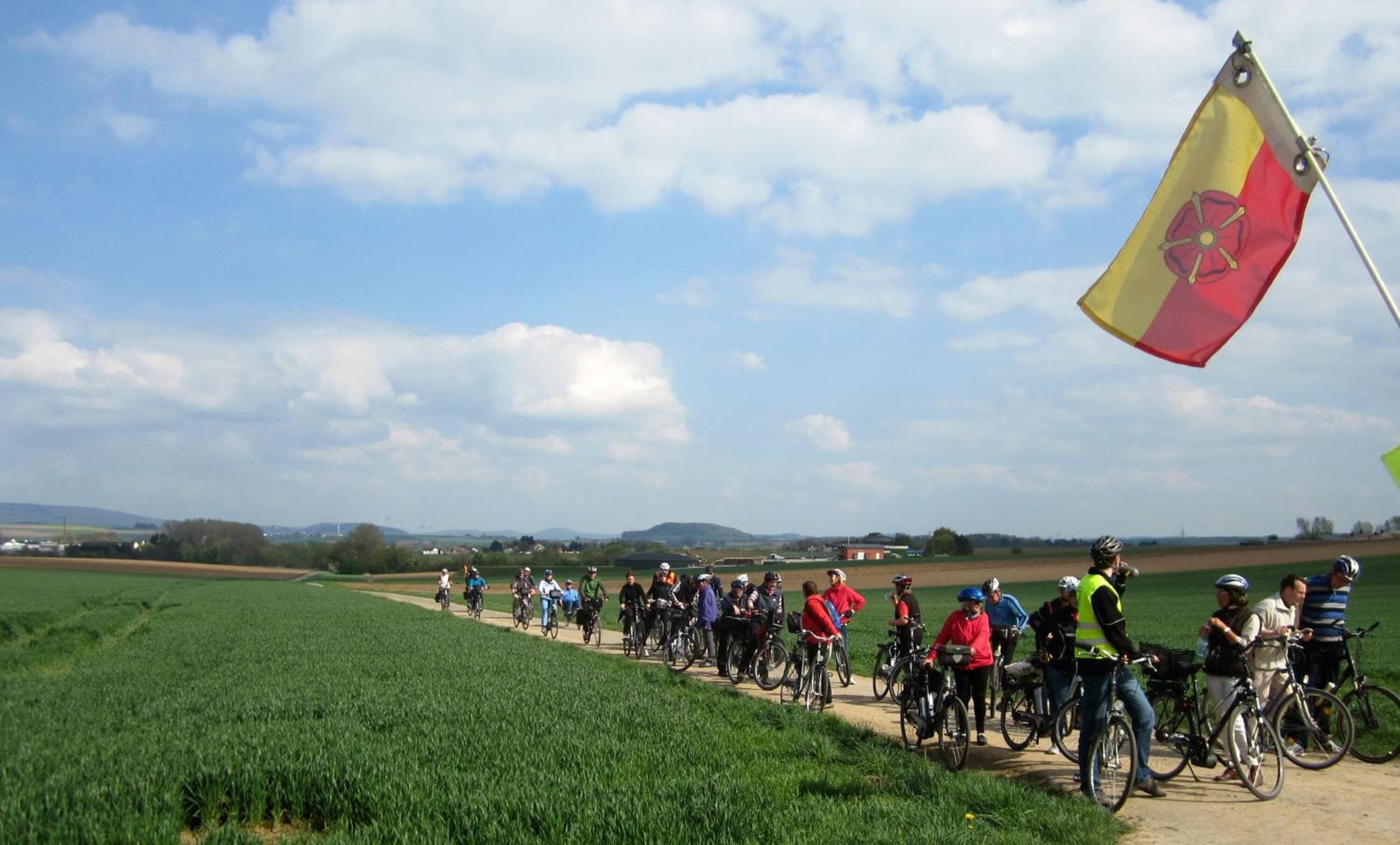 A group of cyclists on a rural path with a flag in the foreground.