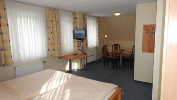 A hotel room with a bed, a desk with a chair, a television, and a small table.