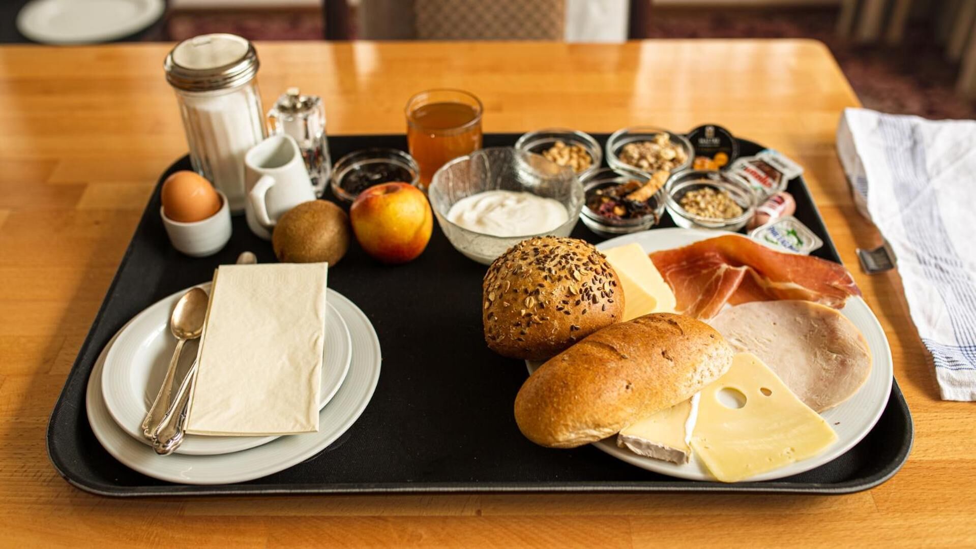 En bakke med morgenmad, indeholdende brød, ost, skinke, æg, frugt og tilbehør.