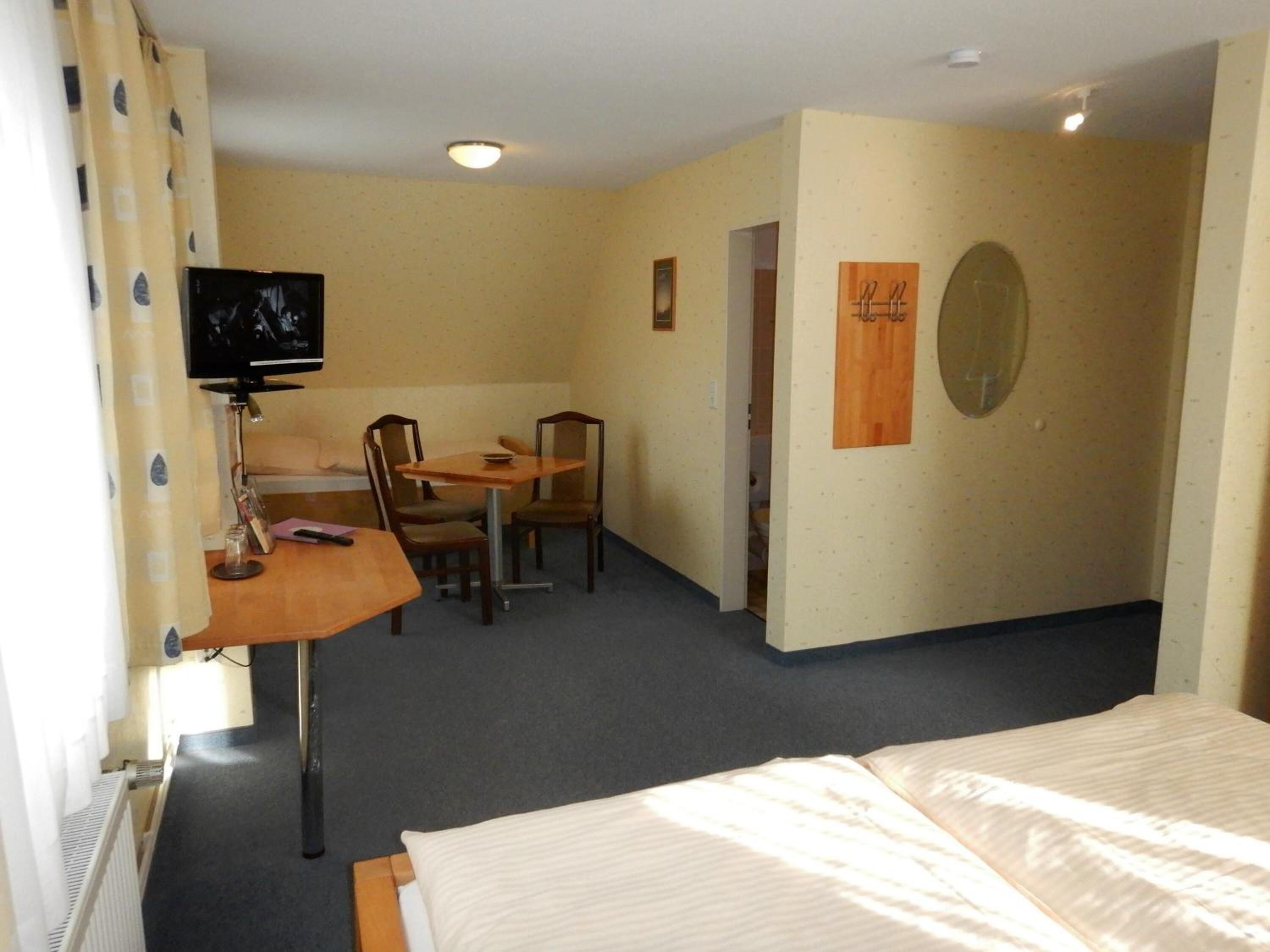 A hotel room with a bed, a desk with a chair, a television, and a coat rack.