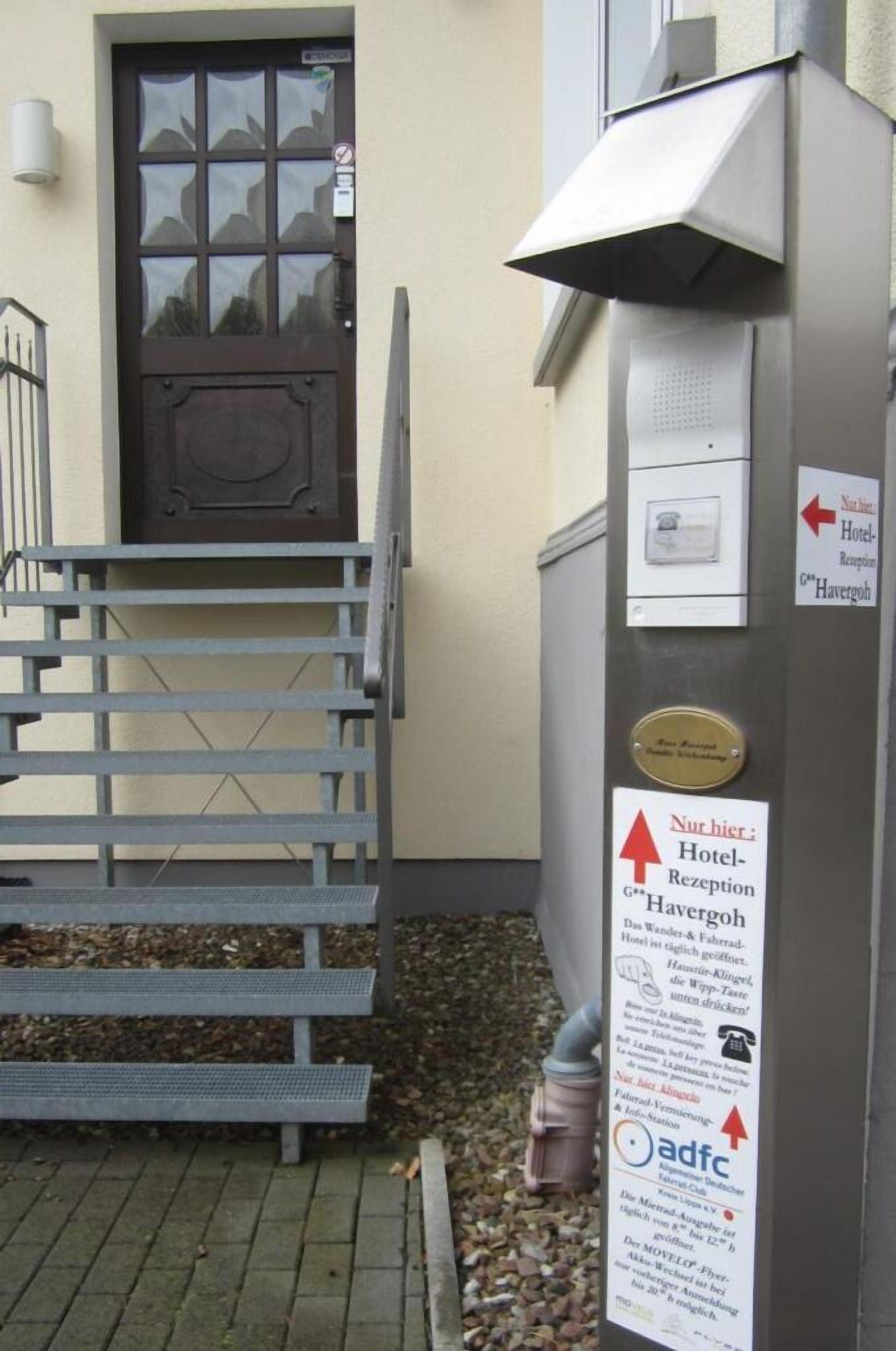 A hotel entrance with a staircase leading to a door, a sign for the hotel reception, and an information board.