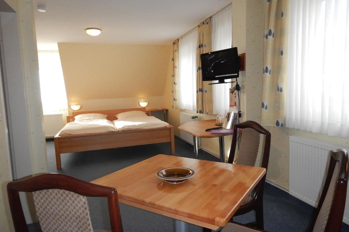 A hotel room with a bed, a desk, a chair, a television, and a window with curtains.