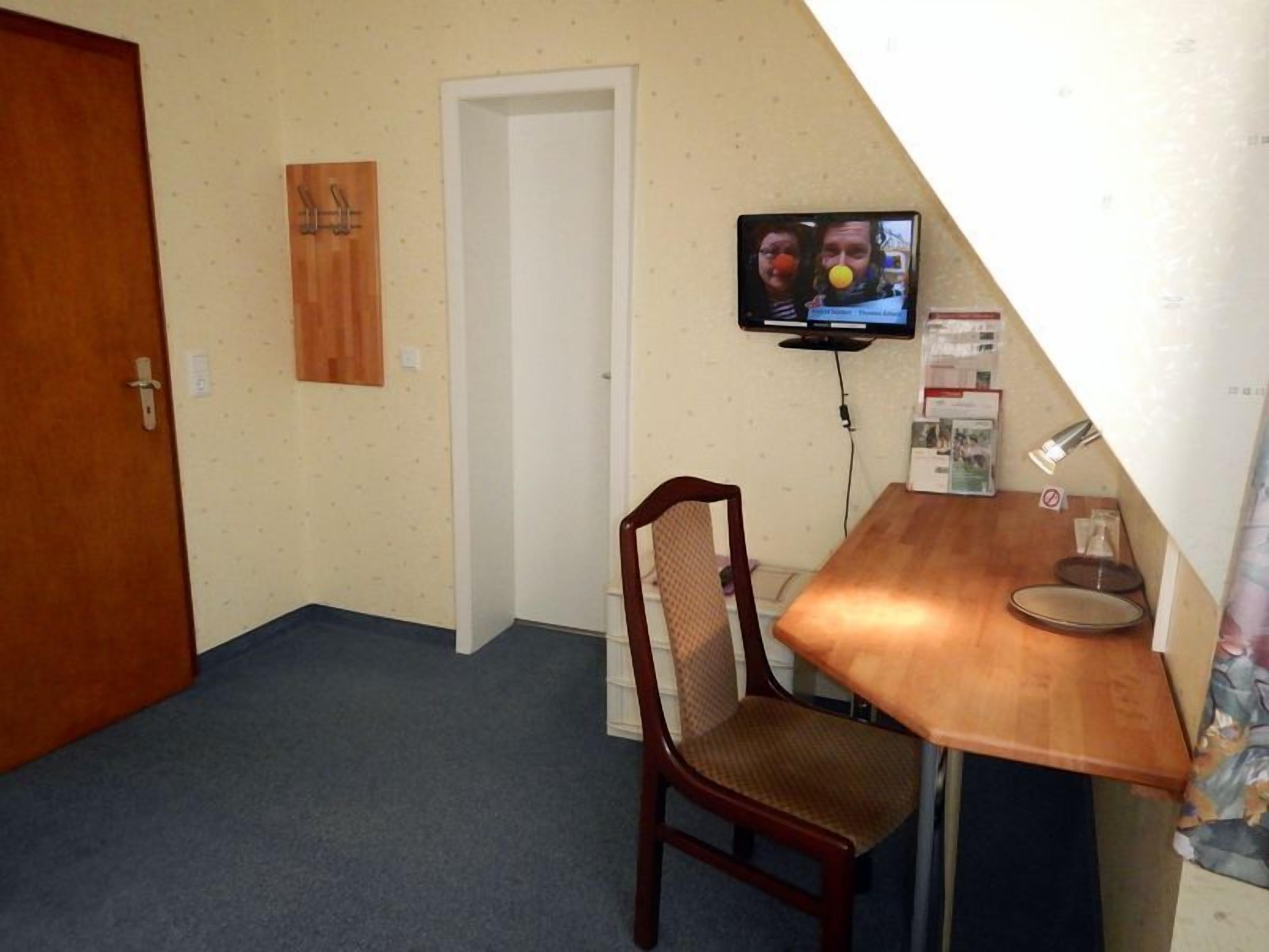 A small room with a wooden desk, a chair, a television mounted on the wall, and a door.