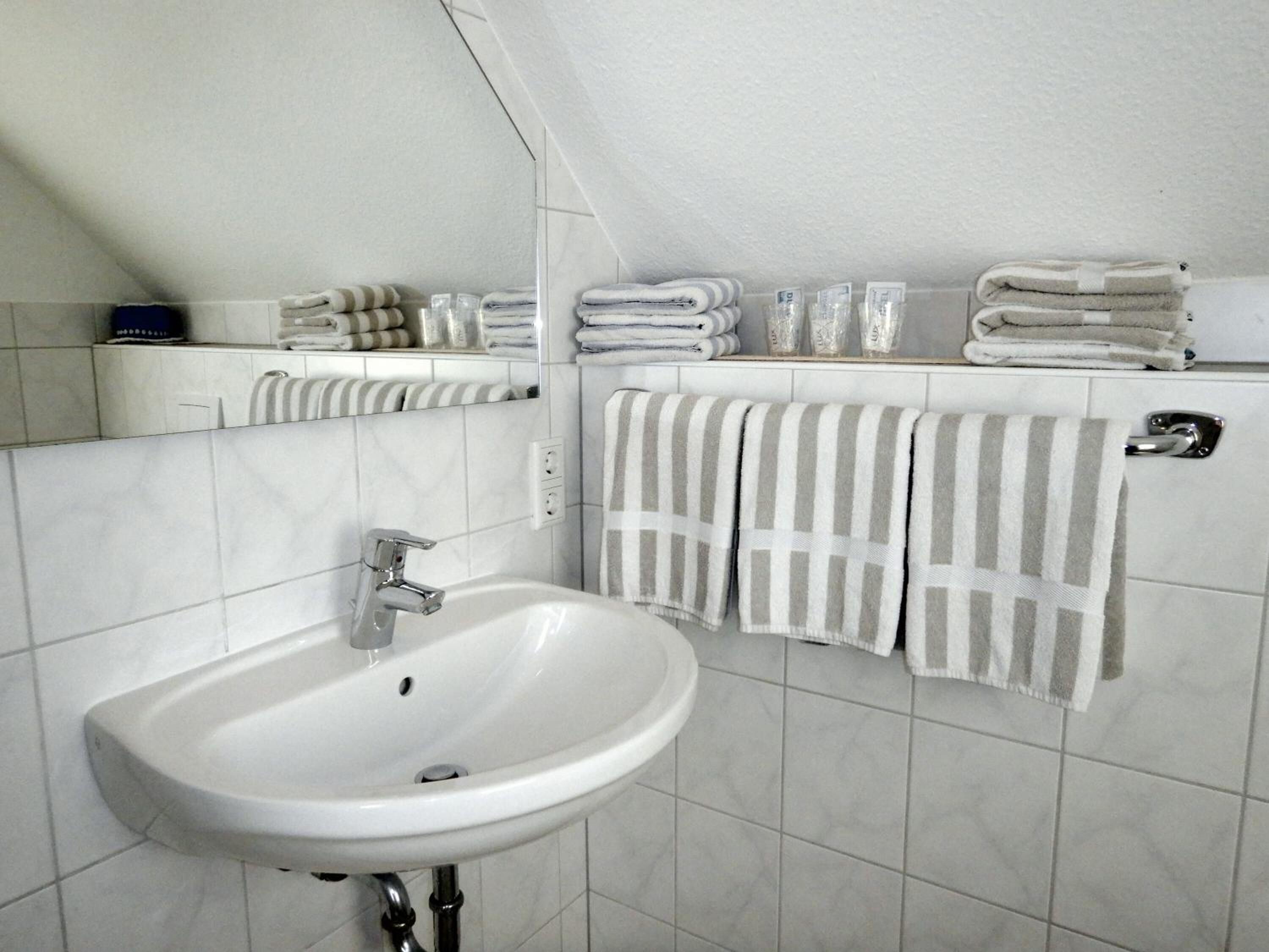 Un baño con un lavamanos blanco, un espejo y varias toallas apiladas en un estante.
