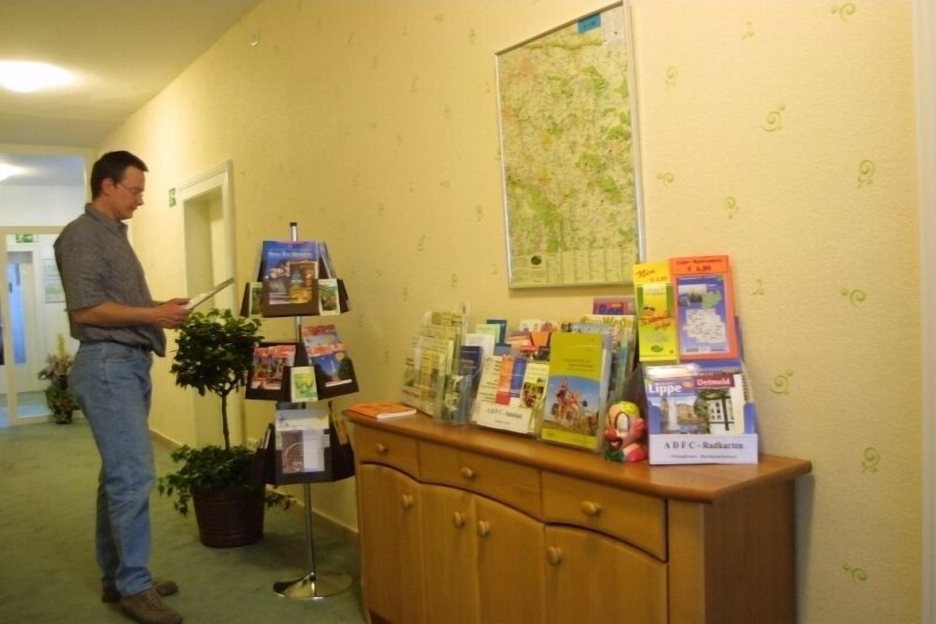 A man standing in a hallway with a map on the wall and a display of brochures and books on a wooden cabinet.
