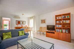 A living room with a sofa, chairs, a coffee table, a bookshelf, a TV, and a dining area with a table and chairs.