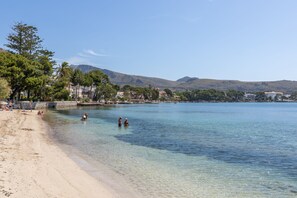 Una playa con agua cristalina, gente nadando y edificios al fondo.